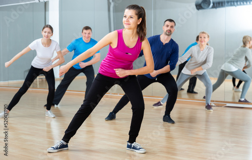 Portrait of young emotional woman doing exercises during group class in dance center