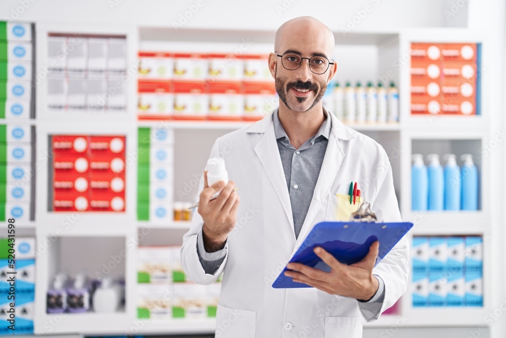 Young hispanic man pharmacist holding clipboard and pills at pharmacy