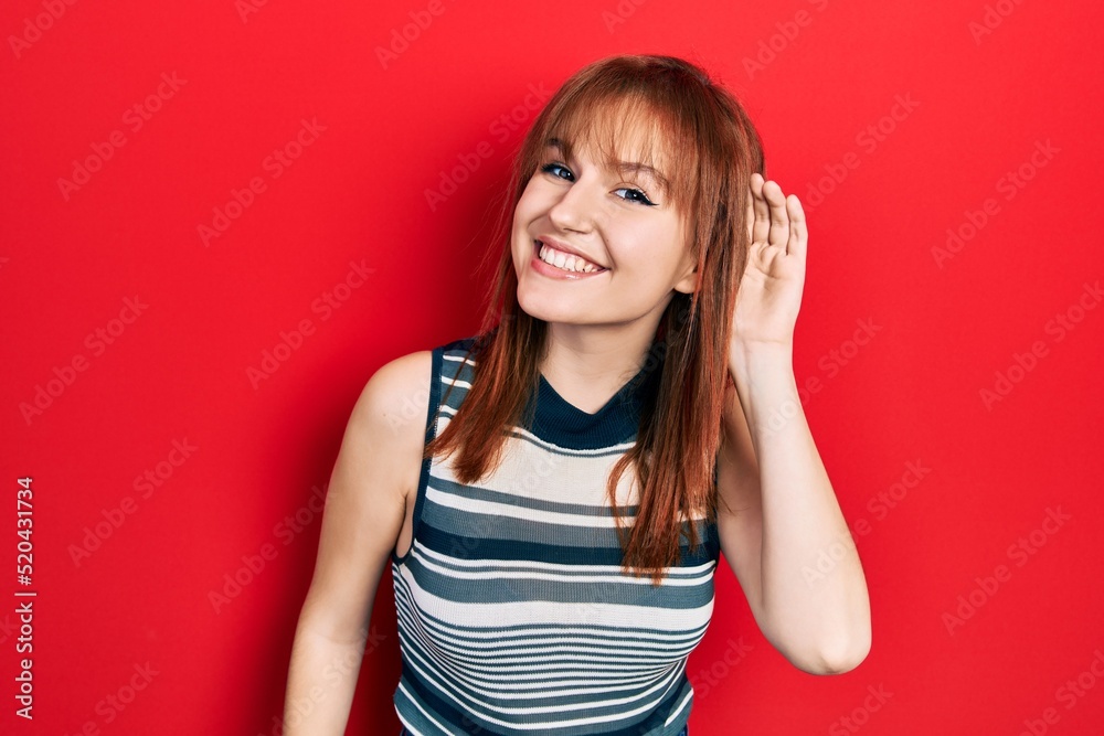 Redhead young woman wearing casual t shirt smiling with hand over ear listening an hearing to rumor or gossip. deafness concept. Redhead young woman wearing casual t shirt smiling with hand over ear listening an hearing to rumor or gossip. deafness concept.