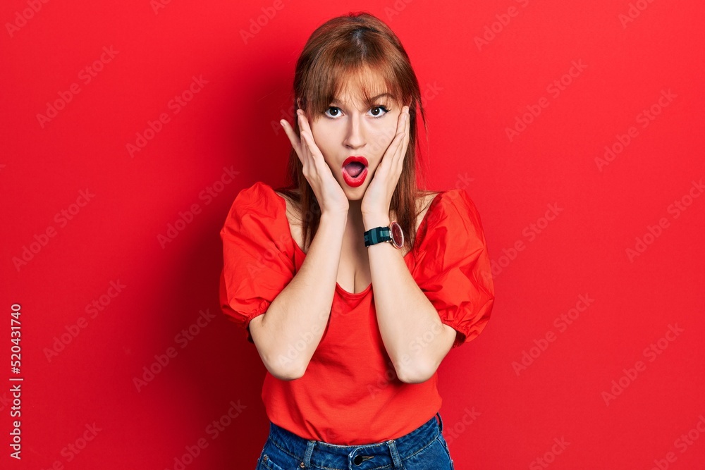 Redhead young woman wearing casual red t shirt afraid and shocked, surprise and amazed expression with hands on face Redhead young woman wearing casual red t shirt afraid and shocked, surprise and amazed expression with hands on face