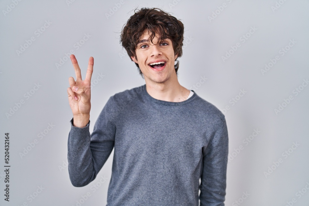 Fototapeta premium Young man standing over isolated background showing and pointing up with fingers number two while smiling confident and happy.