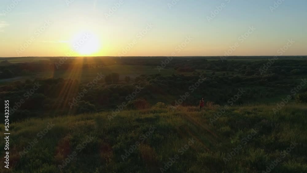 Aerial view mother and son are standing on a mountain cliff hugging watching the sunset or sunrise. Drone shot beautiful summer evening or morning sun in field Aerial view mother and son are standing on a mountain cliff hugging watching the sunset or sunrise. Drone shot beautiful summer evening or morning sun in field