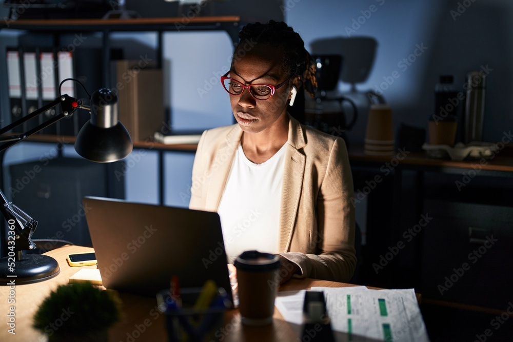 Beautiful black woman working at the office at night relaxed with serious expression on face. simple and natural looking at the camera.