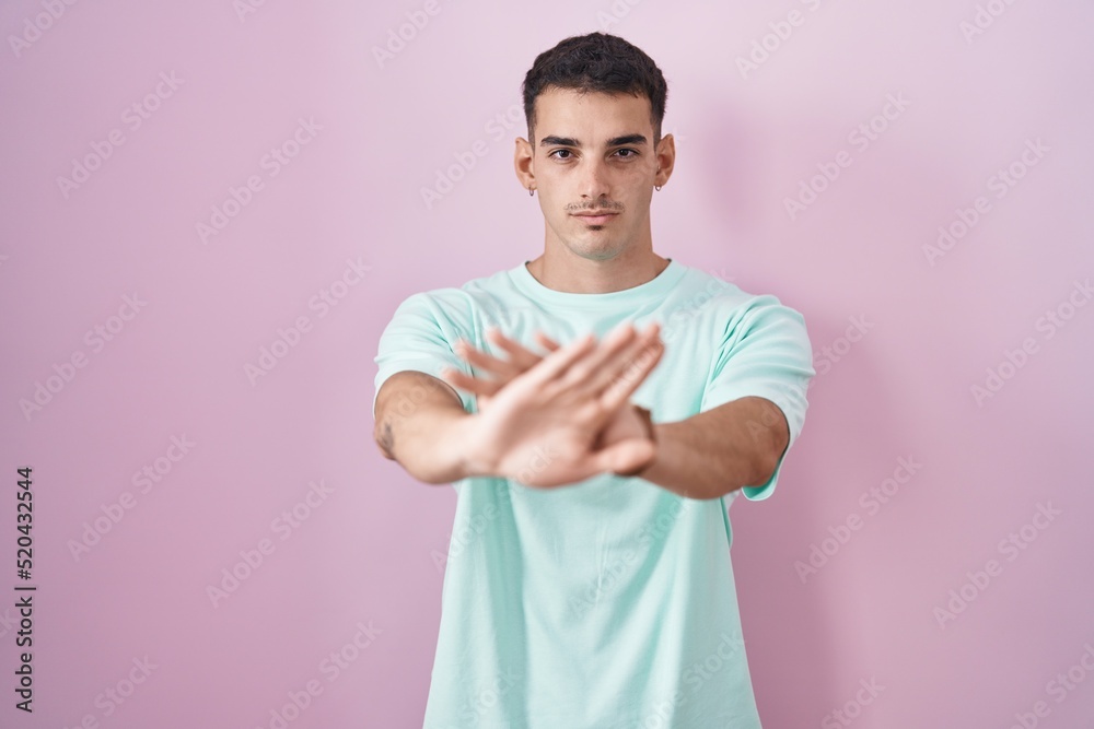 Handsome hispanic man standing over pink background rejection expression crossing arms and palms doing negative sign, angry face Handsome hispanic man standing over pink background rejection expression crossing arms and palms doing negative sign, angry face