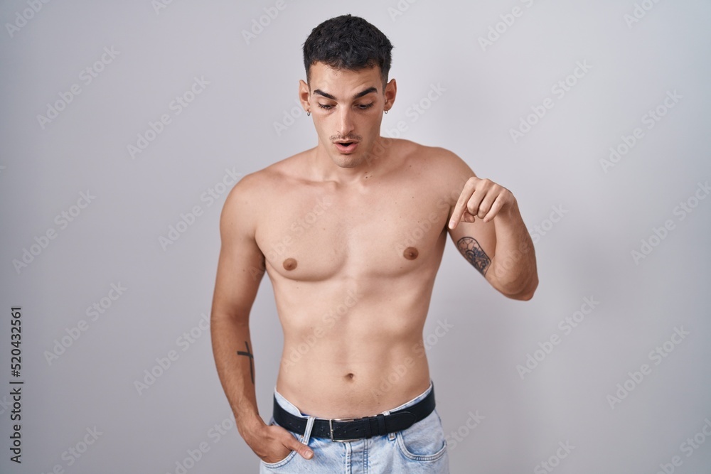 Handsome hispanic man standing shirtless pointing down with fingers showing advertisement, surprised face and open mouth