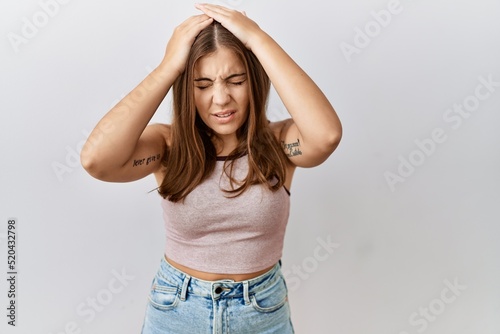 Young brunette woman standing over isolated background suffering from headache desperate and stressed because pain and migraine. hands on head.