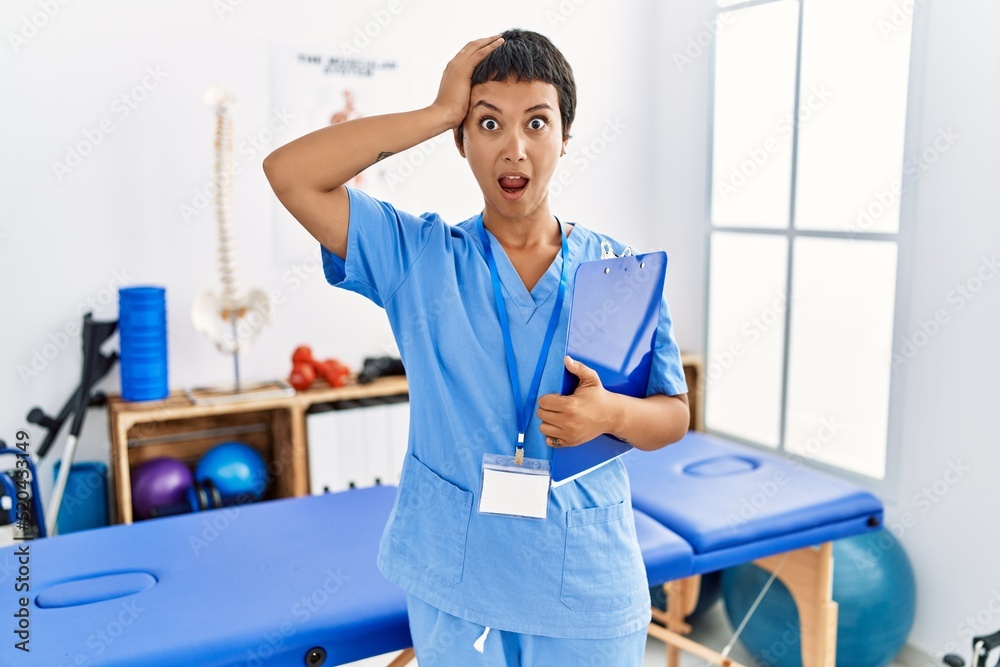 Young hispanic woman with short hair working at pain recovery clinic crazy and scared with hands on head, afraid and surprised of shock with open mouth Young hispanic woman with short hair working at pain recovery clinic crazy and scared with hands on head, afraid and surprised of shock with open mouth