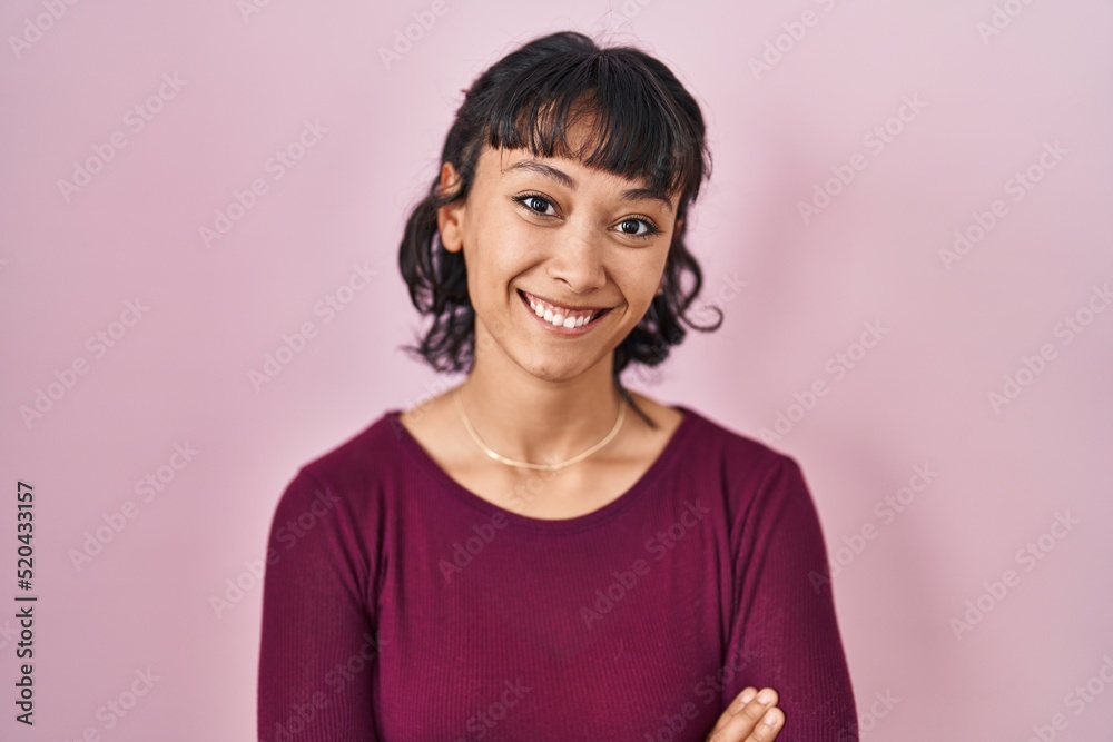 Fototapeta premium Young beautiful woman standing over pink background happy face smiling with crossed arms looking at the camera. positive person.