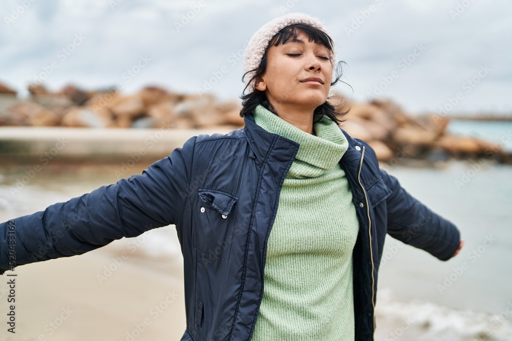 Young beautiful hispanic woman breathing with arms open at seaside Young beautiful hispanic woman breathing with arms open at seaside