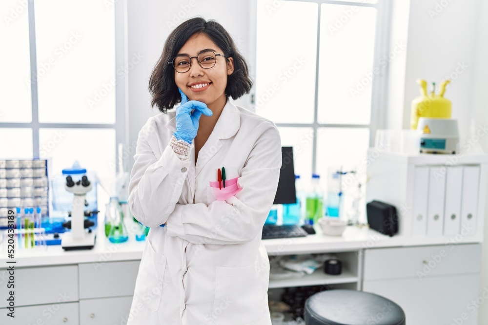 Young latin woman wearing scientist uniform standing at laboratory