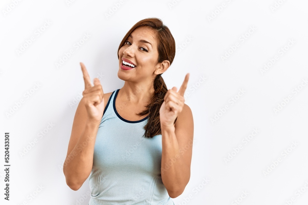 Young latin woman wearing sporty clothes over isolated background pointing fingers to camera with happy and funny face. good energy and vibes. Young latin woman wearing sporty clothes over isolated background pointing fingers to camera with happy and funny face. good energy and vibes.