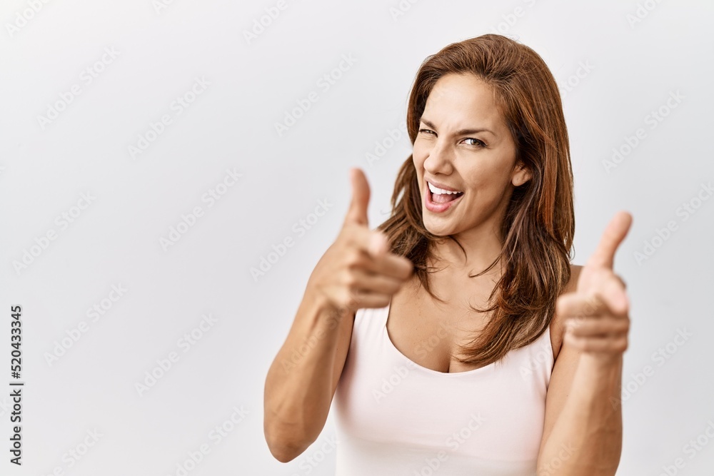 Middle age hispanic woman standing over isolated background pointing fingers to camera with happy and funny face. good energy and vibes. Middle age hispanic woman standing over isolated background pointing fingers to camera with happy and funny face. good energy and vibes.