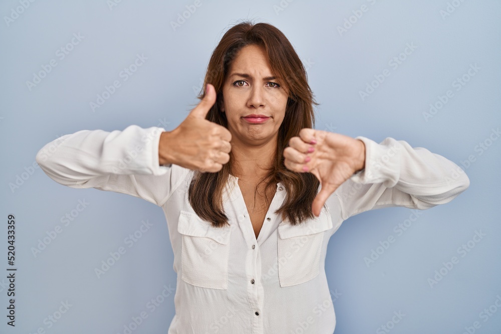 Hispanic woman standing over isolated background doing thumbs up and down, disagreement and agreement expression. crazy conflict