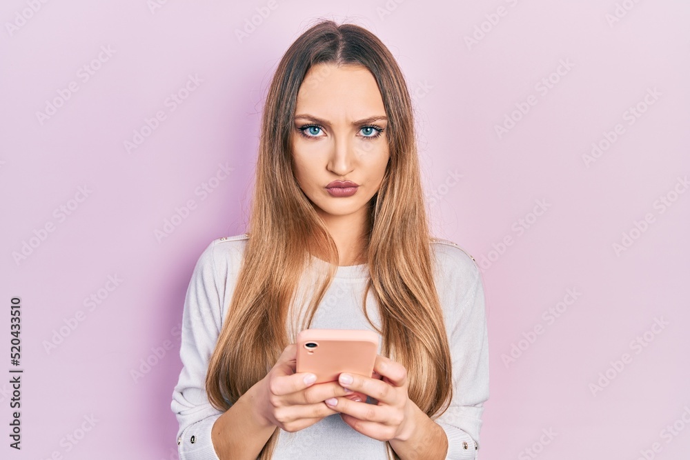 Young blonde girl using smartphone typing message skeptic and nervous, frowning upset because of problem. negative person. Young blonde girl using smartphone typing message skeptic and nervous, frowning upset because of problem. negative person.