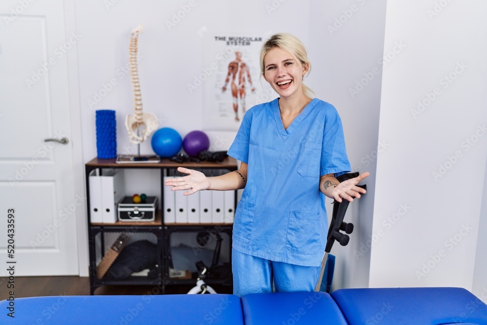Young physiotherapist woman working at pain recovery clinic smiling cheerful with open arms as friendly welcome, positive and confident greetings Young physiotherapist woman working at pain recovery clinic smiling cheerful with open arms as friendly welcome, positive and confident greetings