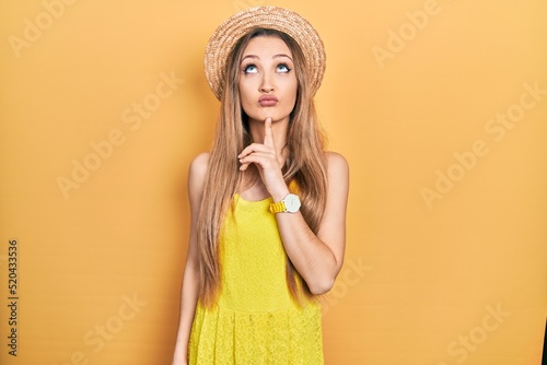 Young blonde girl wearing summer hat thinking concentrated about doubt with finger on chin and looking up wondering