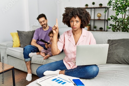 Mother of interracial family working using computer laptop at home pointing up looking sad and upset, indicating direction with fingers, unhappy and depressed.