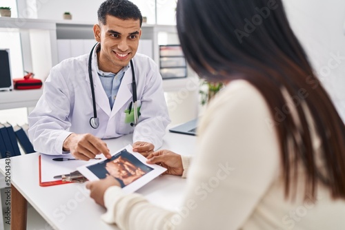 Young latin couple doctor and patient looking baby ecography at clinic