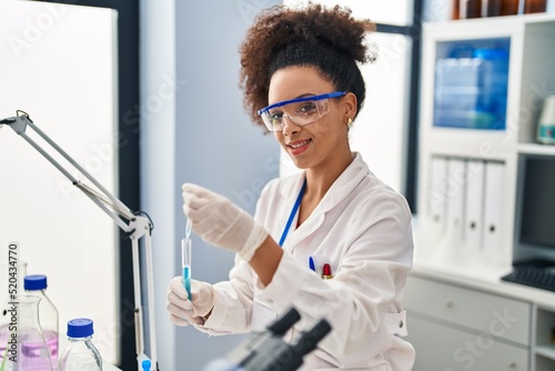 Young african american woman wearing scientist uniform using pipette working at laboratory