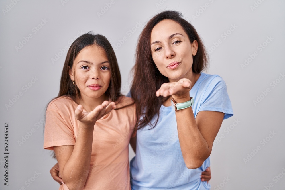 Young mother and daughter standing over white background looking at the camera blowing a kiss with hand on air being lovely and sexy. love expression. Young mother and daughter standing over white background looking at the camera blowing a kiss with hand on air being lovely and sexy. love expression.