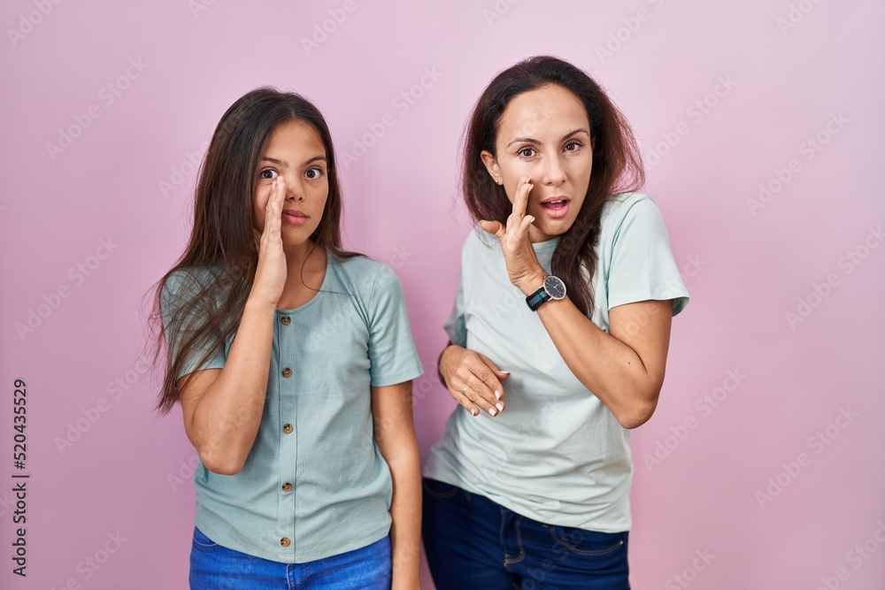 Young mother and daughter standing over pink background hand on mouth telling secret rumor, whispering malicious talk conversation Young mother and daughter standing over pink background hand on mouth telling secret rumor, whispering malicious talk conversation