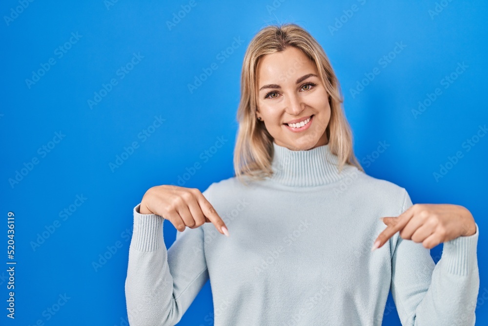 Fototapeta premium Young caucasian woman standing over blue background looking confident with smile on face, pointing oneself with fingers proud and happy.