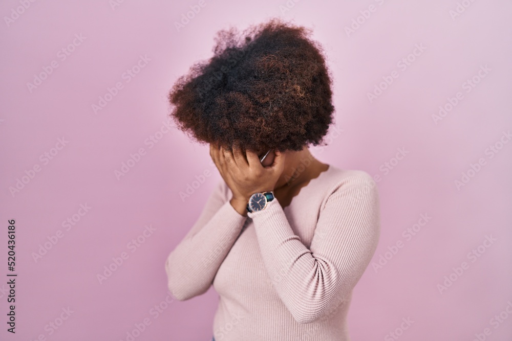 Young african american woman standing over pink background with sad expression covering face with hands while crying. depression concept. Young african american woman standing over pink background with sad expression covering face with hands while crying. depression concept.