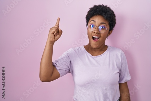 Young african american woman standing over pink background pointing finger up with successful idea. exited and happy. number one.