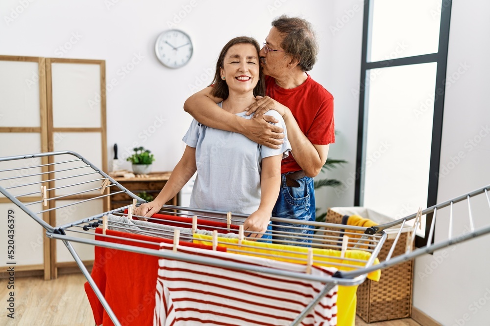 Obraz premium Middle age man and woman couple hugging and hanging clothes on clothesline at laundry