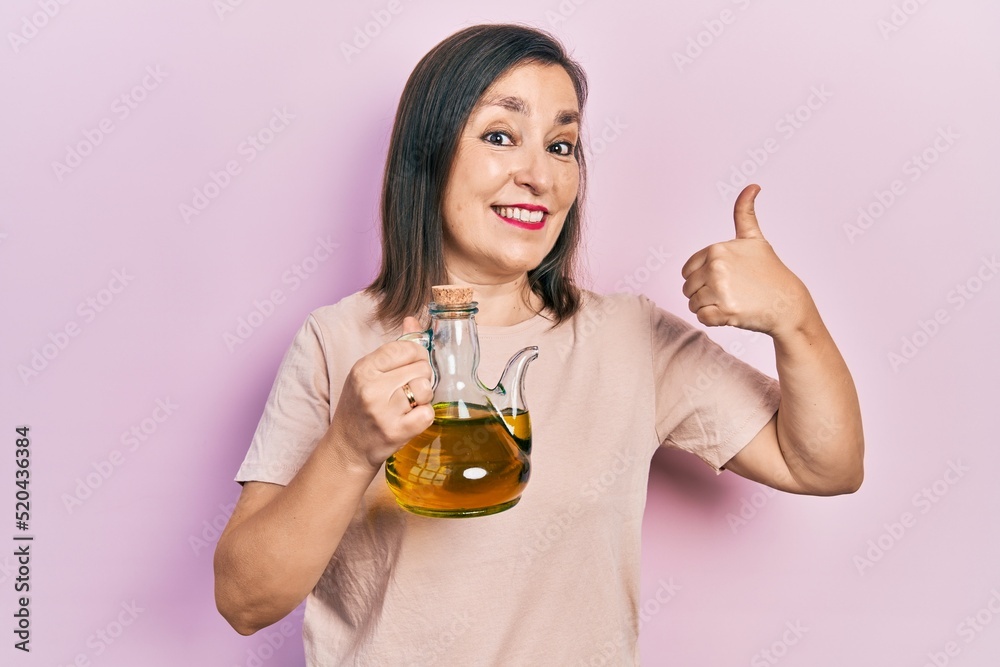 Middle age hispanic woman holding olive oil can smiling happy and positive, thumb up doing excellent and approval sign Middle age hispanic woman holding olive oil can smiling happy and positive, thumb up doing excellent and approval sign
