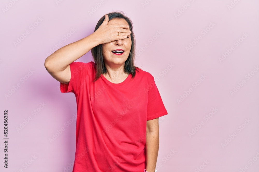 Middle age hispanic woman wearing casual clothes smiling and laughing with hand on face covering eyes for surprise. blind concept. Middle age hispanic woman wearing casual clothes smiling and laughing with hand on face covering eyes for surprise. blind concept.