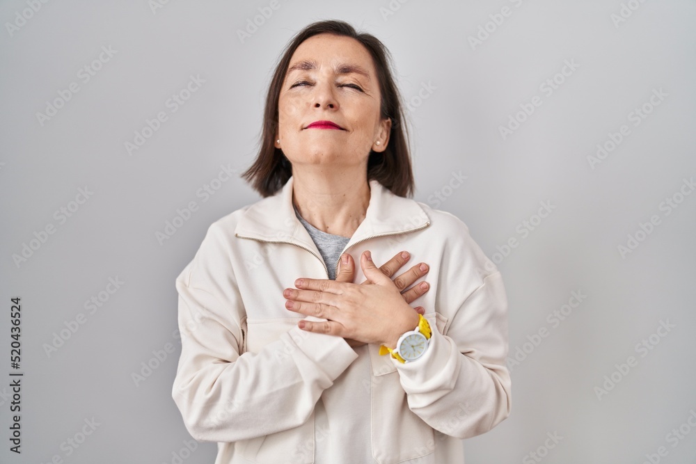 Middle age hispanic woman standing over isolated background smiling with hands on chest with closed eyes and grateful gesture on face. health concept. Middle age hispanic woman standing over isolated background smiling with hands on chest with closed eyes and grateful gesture on face. health concept.