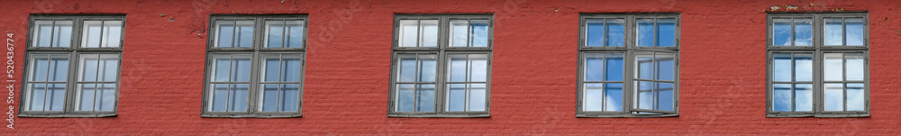 Row of square windows in a red brick wall, blue sky and clouds reflecting in the glass
Row of square windows in a red brick wall, blue sky and clouds reflecting in the glass