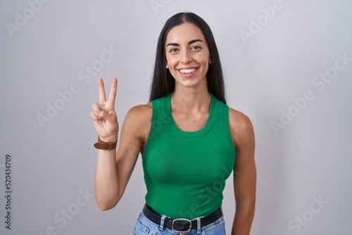 Young woman standing over isolated background showing and pointing up with fingers number two while smiling confident and happy.