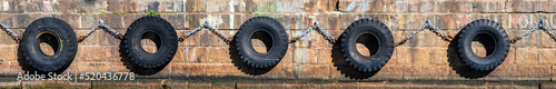 Photography Row of old tires chained together against a stone pier as ship bumpers
