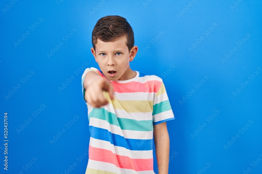 Young caucasian kid standing over blue background pointing displeased and frustrated to the camera, angry and furious with you Young caucasian kid standing over blue background pointing displeased and frustrated to the camera, angry and furious with you