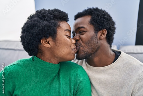 African american man and woman couple sitting together kissing at home