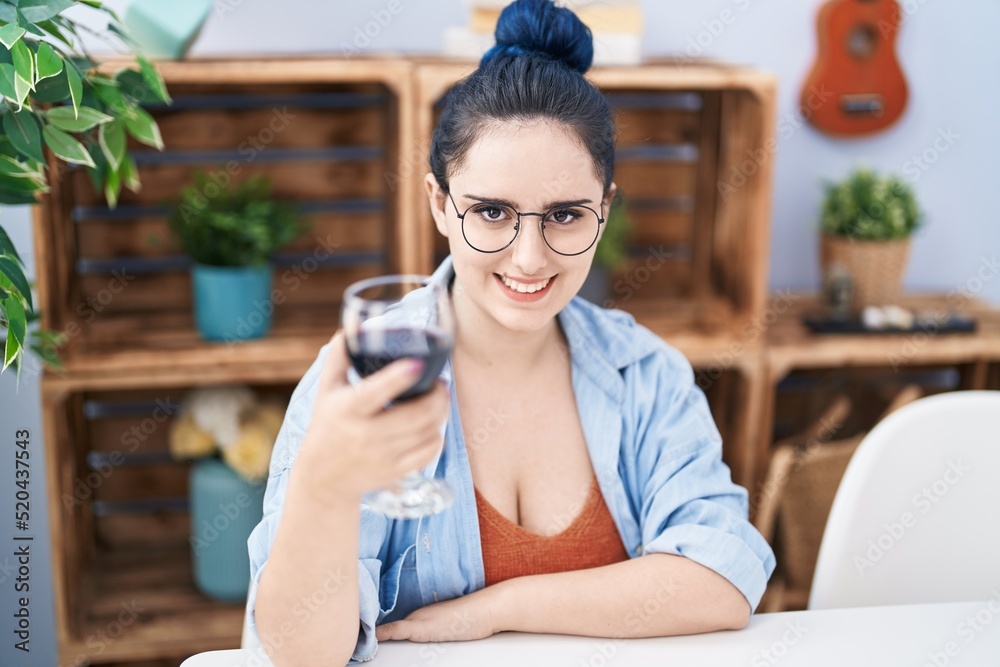 Fototapeta premium Young caucasian woman drinking glass of wine sitting on table at home