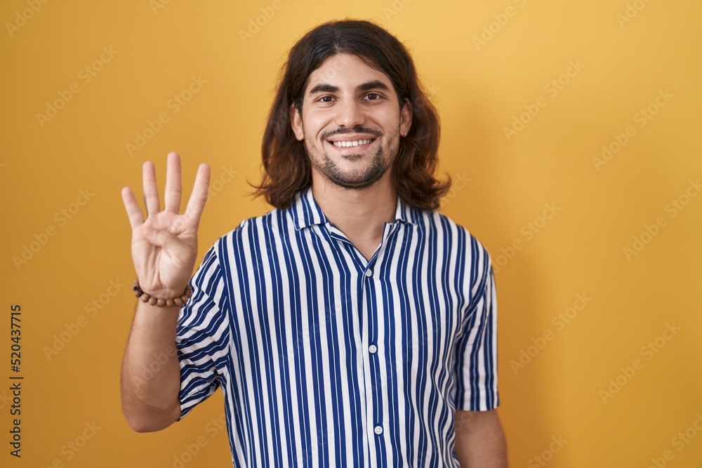 Hispanic man with long hair standing over yellow background showing and pointing up with fingers number four while smiling confident and happy. Hispanic man with long hair standing over yellow background showing and pointing up with fingers number four while smiling confident and happy.