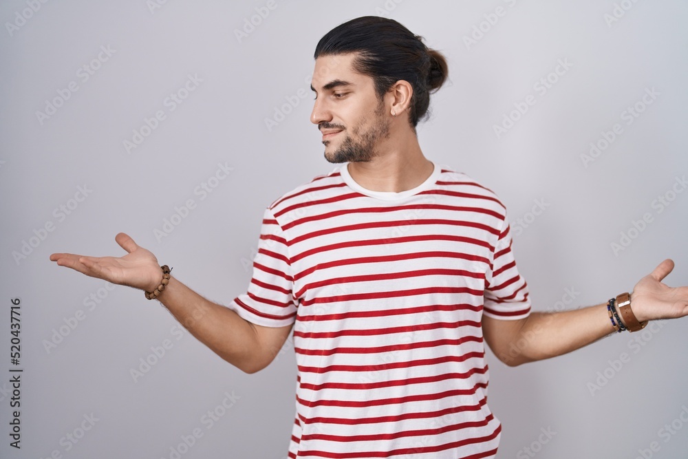 Hispanic man with long hair standing over isolated background smiling showing both hands open palms, presenting and advertising comparison and balance Hispanic man with long hair standing over isolated background smiling showing both hands open palms, presenting and advertising comparison and balance