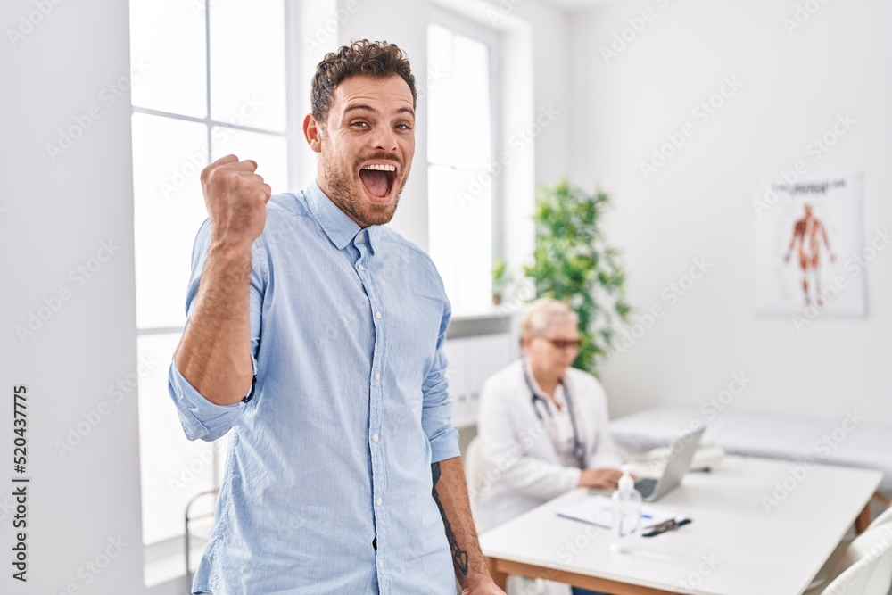 Fototapeta premium Hispanic man at doctor clinic screaming proud, celebrating victory and success very excited with raised arm