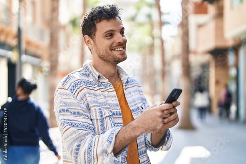 Young hispanic man smiling confident using smartphone at street