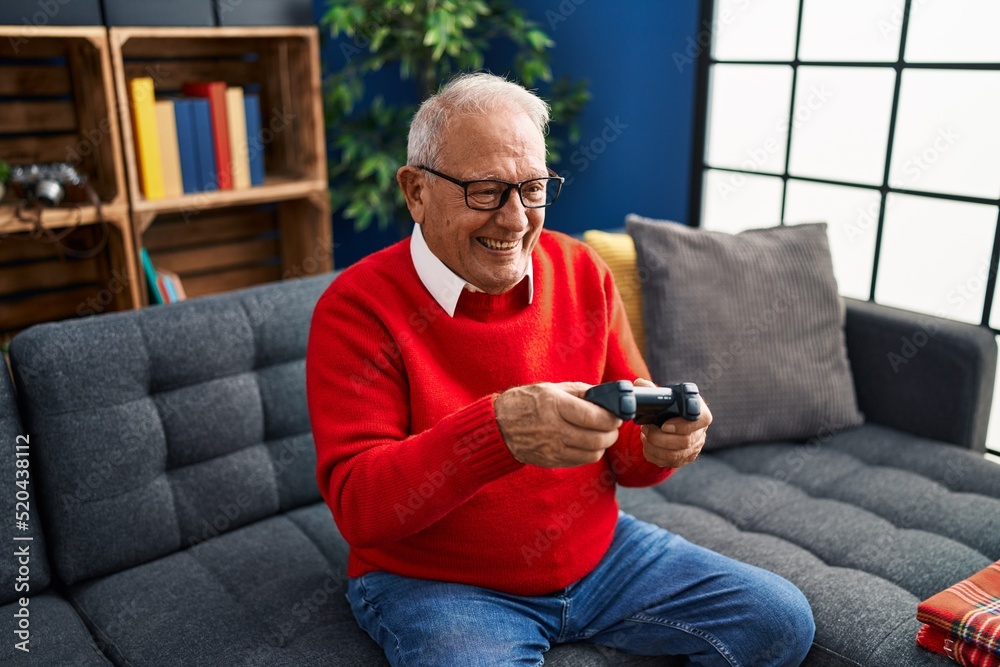 Senior man playing video game sitting on sofa at home