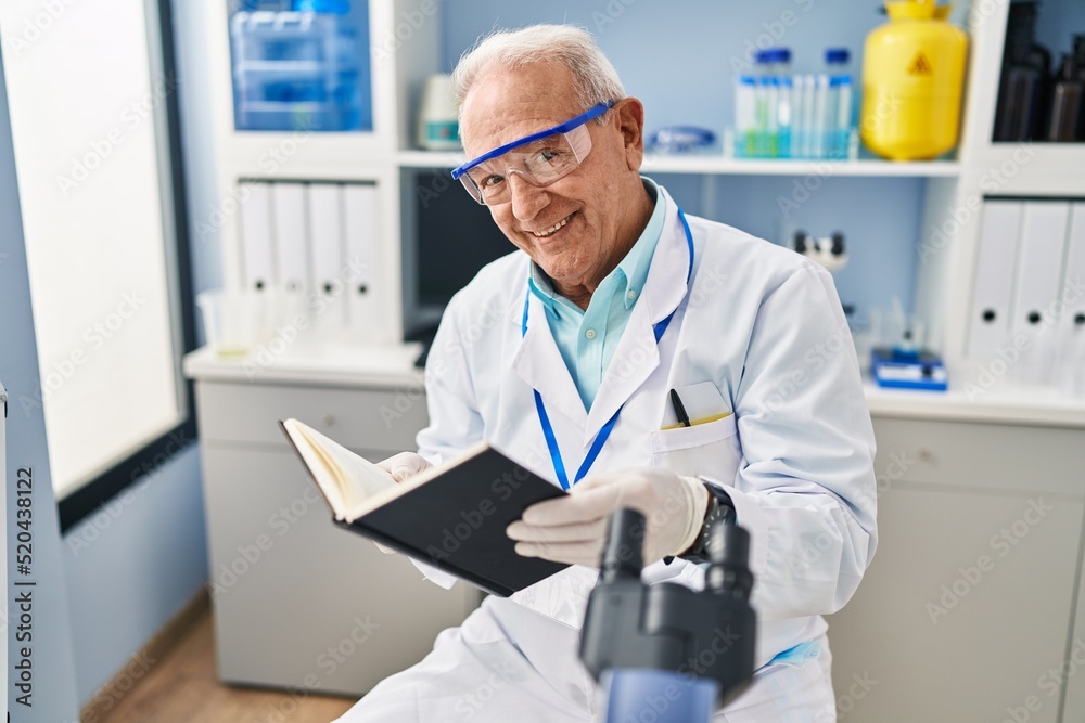 Senior man wearing scientist uniform reading book at laboratory