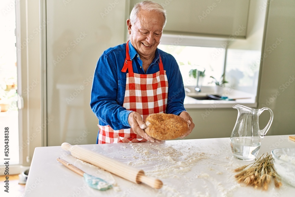 Senior man smiling confident holding homemade bread at kitchen