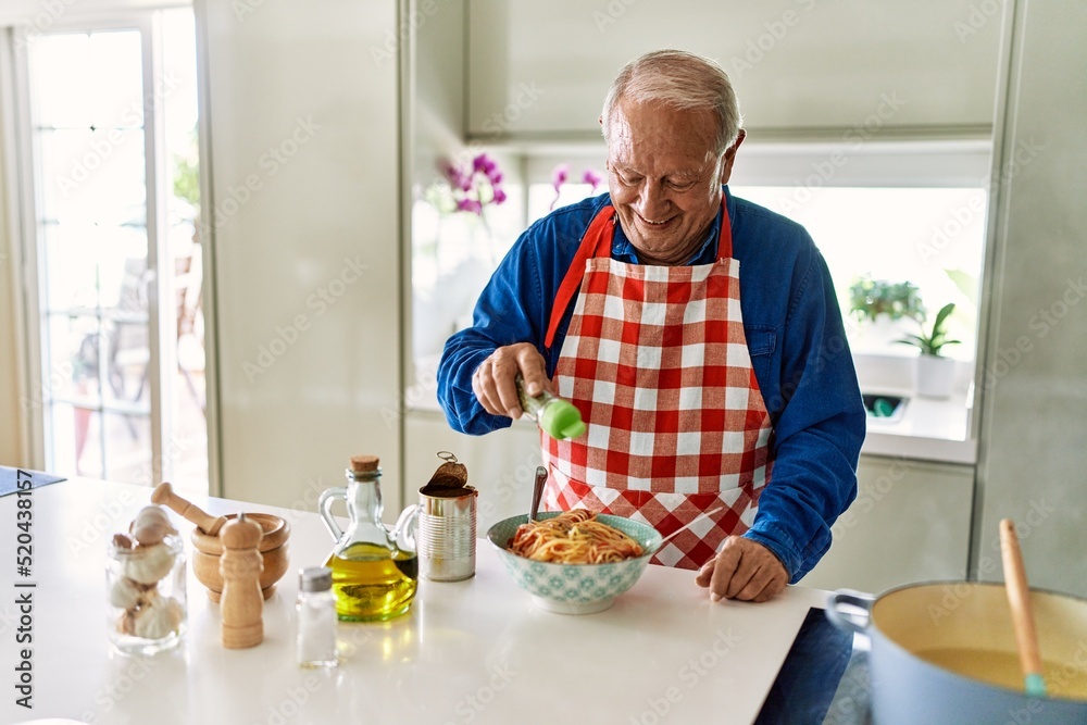 Senior man smiling confident pouring oregano on spaghetti at kitchen Senior man smiling confident pouring oregano on spaghetti at kitchen