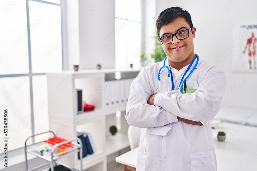 Down syndrome man wearing doctor uniform standing with arms crossed gesture at clinic Down syndrome man wearing doctor uniform standing with arms crossed gesture at clinic