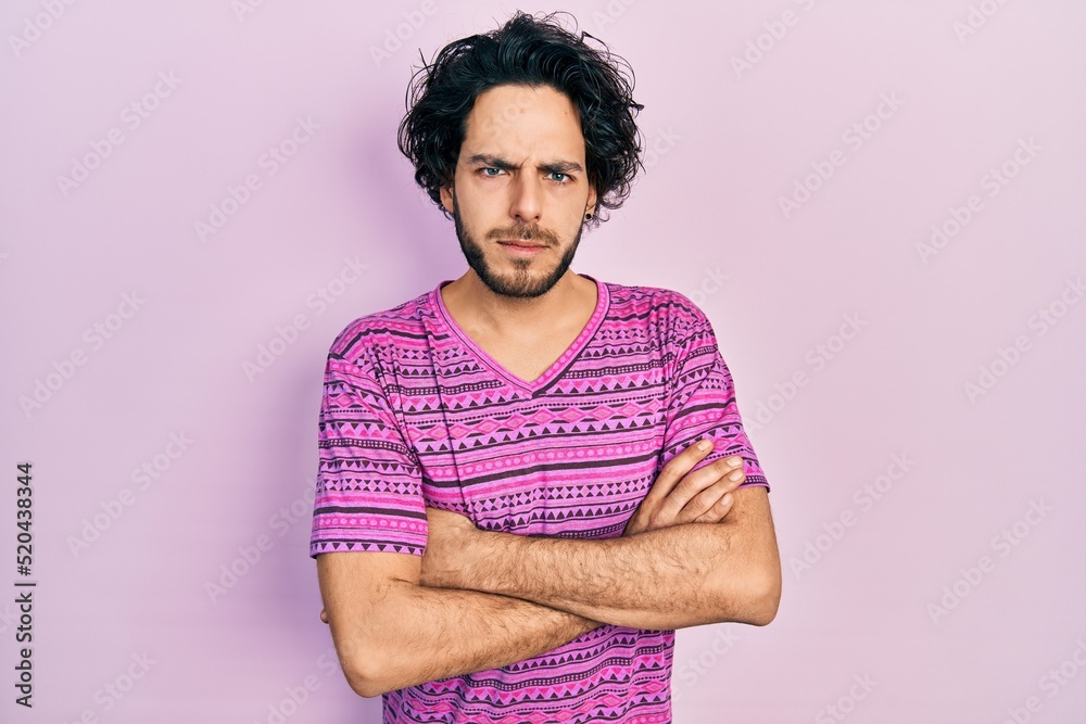 Handsome hispanic man wearing casual pink t shirt skeptic and nervous, disapproving expression on face with crossed arms. negative person. Handsome hispanic man wearing casual pink t shirt skeptic and nervous, disapproving expression on face with crossed arms. negative person.