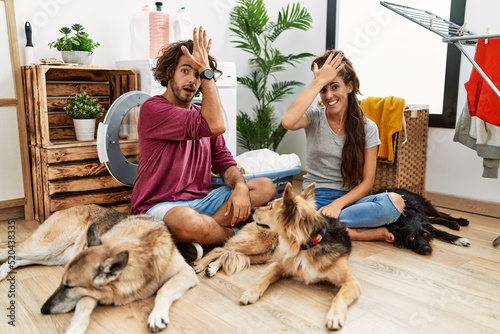 Photography Young hispanic couple doing laundry with dogs surprised with hand on head for mistake, remember error