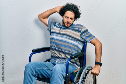Handsome hispanic man sitting on wheelchair stretching back, tired and relaxed, sleepy and yawning for early morning © Krakenimages.com